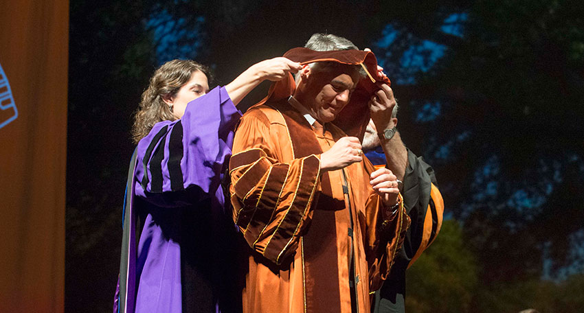 Professors Maria Juenger and William Beckner help President Fenves don the presidential regalia.