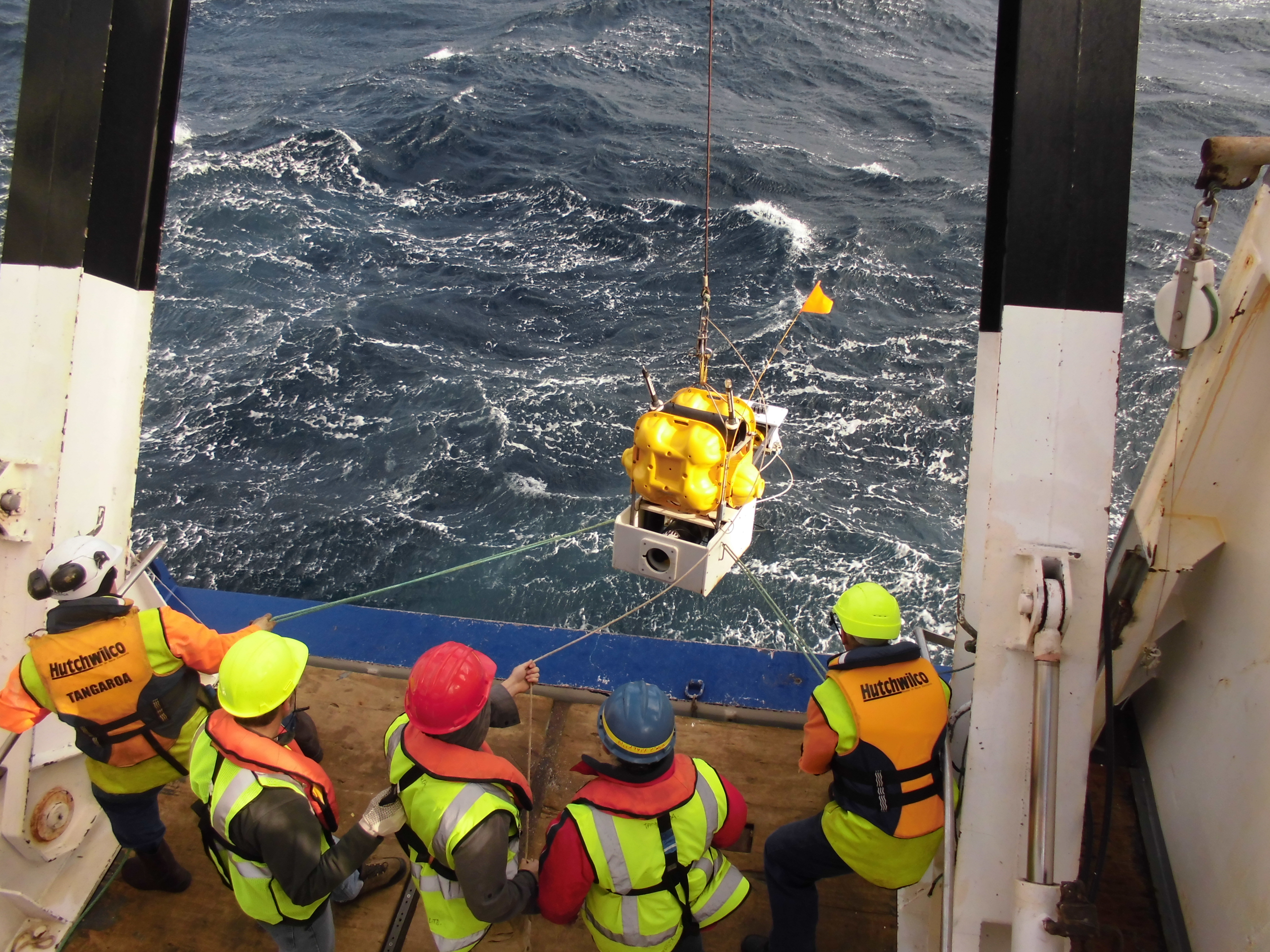 Scientists deploy an ocean bottom seismometer and absolute pressure gauge.