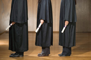 Three robed students standing with their diplomas in hand.