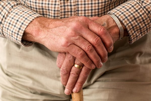 Elderly man with his hands crossed resting them on a cane.