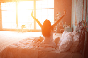 A woman in bed, stretching as the morning sun glows on her.