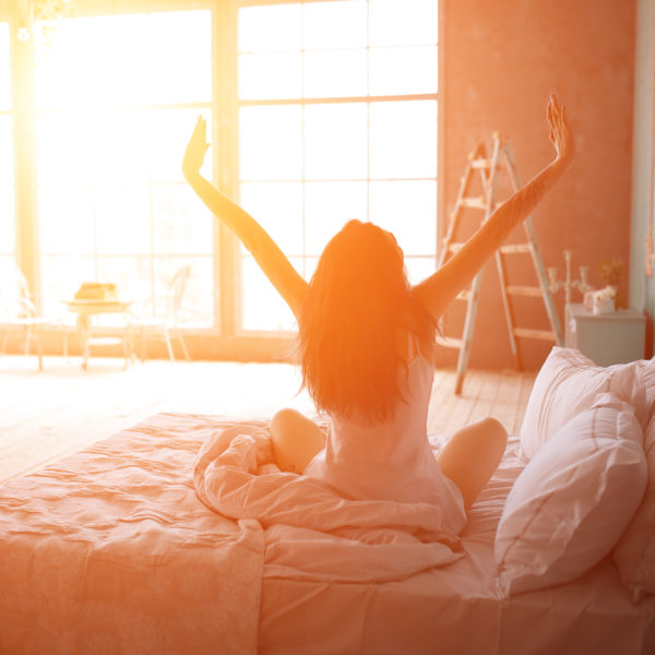 A woman in bed, stretching as the morning sun glows on her.