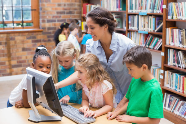 A teacher and students looking at a computer in library at the elementary school