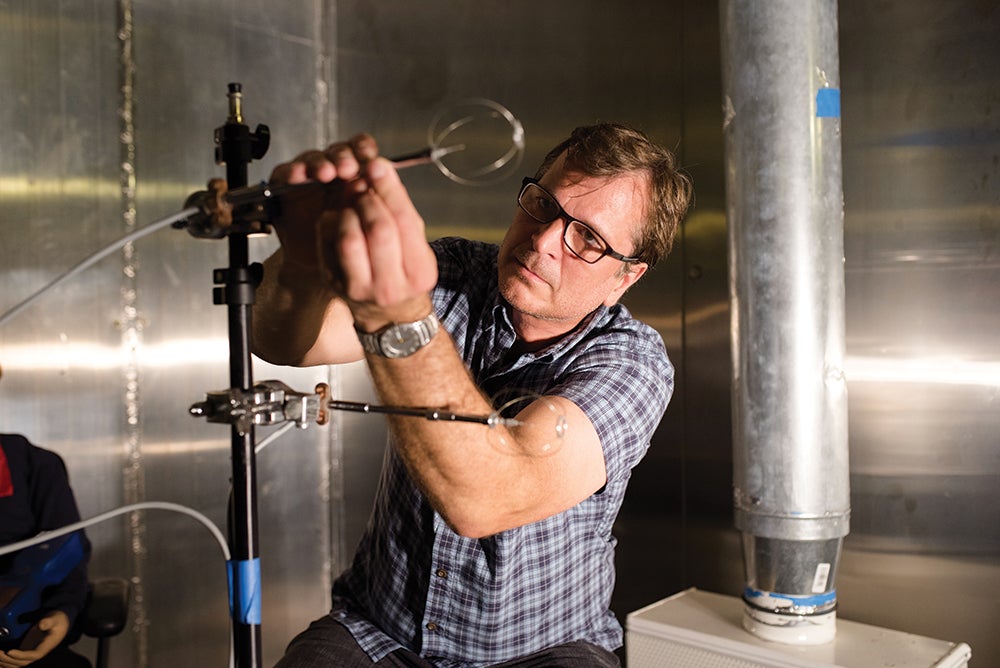A man with glasses adjust some scientific measuring instruments attached to a rod.