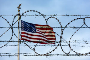 A U.S. flag blows in the wind behind razor wire