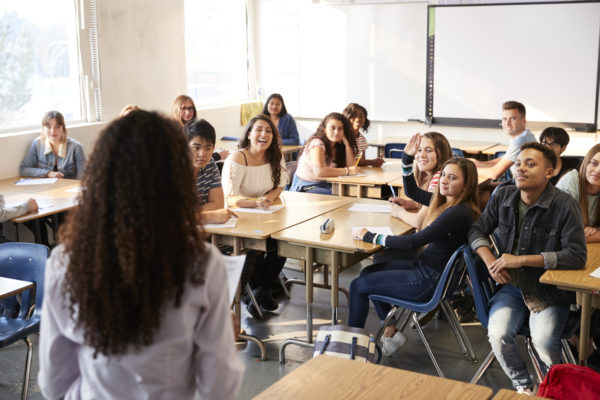Female High School Teacher Standing At Front Of Class Teaching Lesson