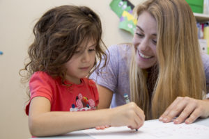 Woman encouraging little girl to color with crayon