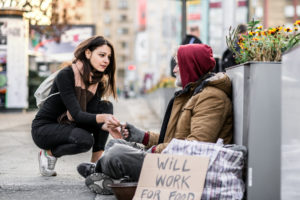 A young woman giving money to homeless man sitting