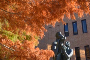 The McCombs School Family statue by Charles Umlauf, framed by rust-colored cypress trees.