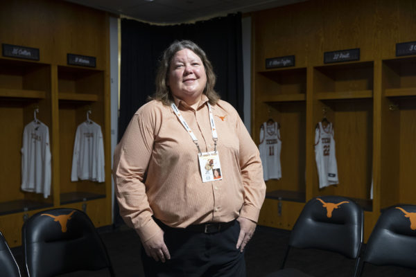 A woman in a burnt orange shirt stands in a locker room.