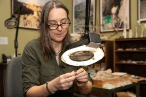 A woman examines a small fossil using a magnifier.