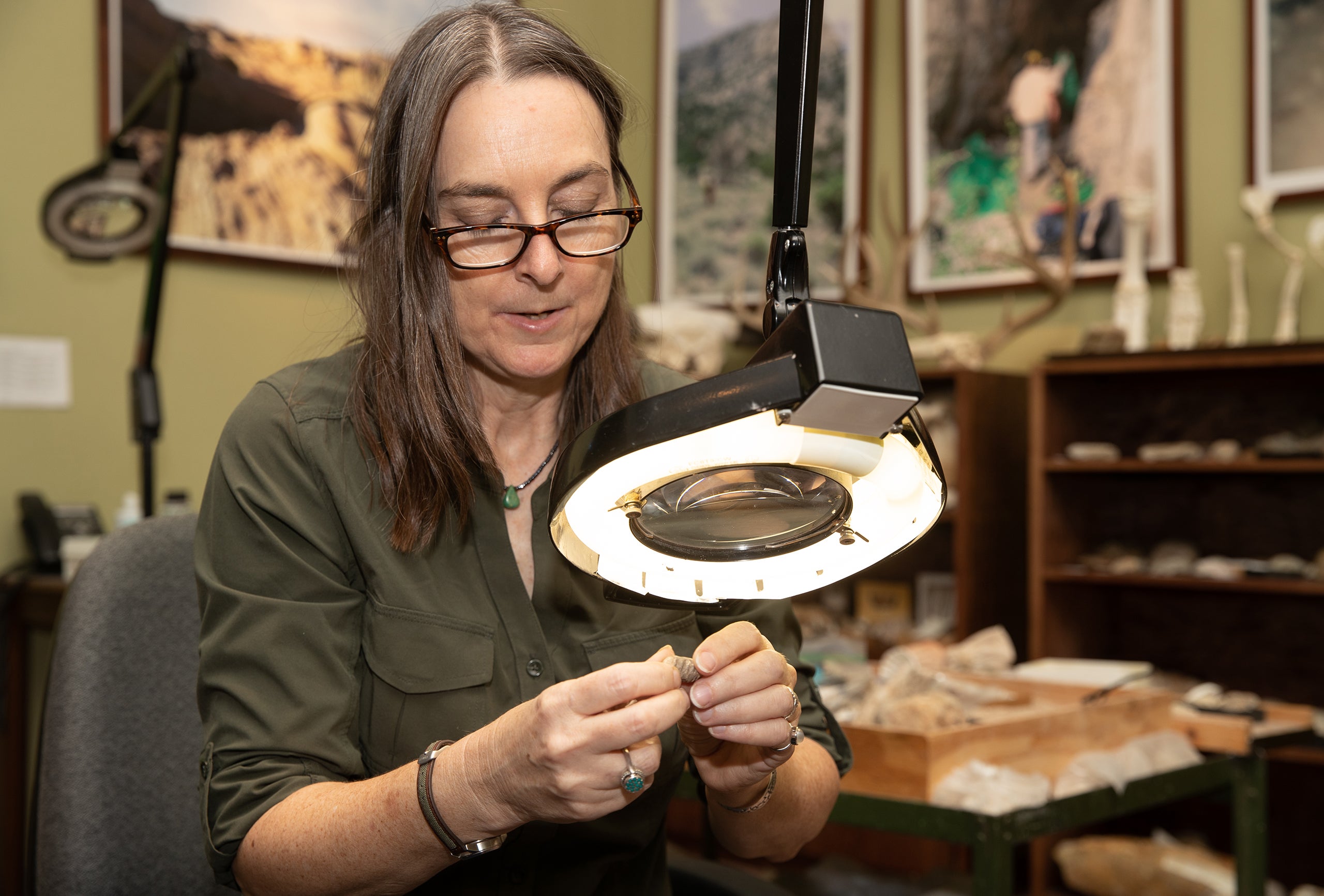 A woman examines a small fossil using a magnifier.