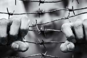 Blurred background with a screaming man face which trying to break the barbed wire with his hands