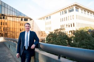 Jay Hartzell standing on walkway on campus, outdoors, suit, tie, glass building behind