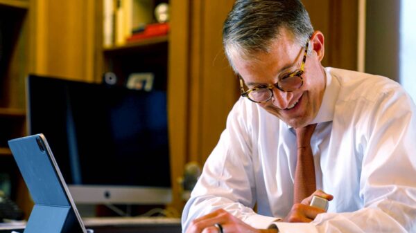 President Jay Hartzell, sitting at desk, orange tie, smile, glasses, tablet, working