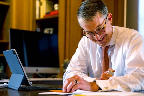 President Jay Hartzell, sitting at desk, orange tie, smile, glasses, tablet, working