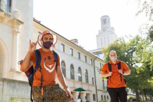 students, hook 'em horns sign, burnt orange shirts, backpacks, masks, tower