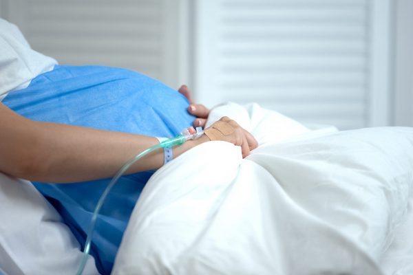 Pregnant woman holding blanket, feeling abdominal pain, risk of miscarriage