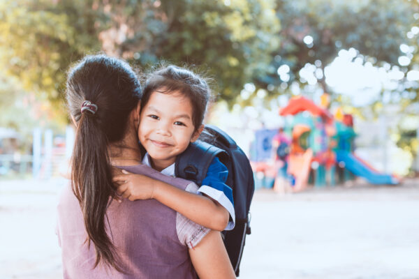 Back to school. Cute asian pupil girl with backpack hugging her mother in the playground before go to classroom in the school.