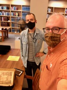 Selfie of two men in masks with old book