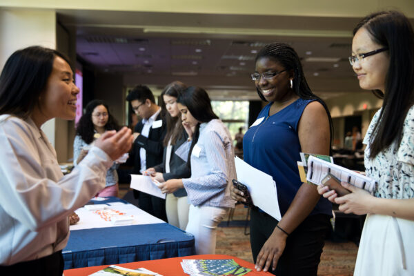 Students visit with someone sitting at a table in a career fair