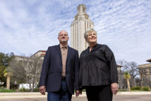 A couple stand on the plaza in front of UT's Tower, gazing upward at the blue sky.
