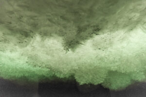 Underwater photo of the underside of an ice shelf. The ice is greenish and rough, like heaps of snow.