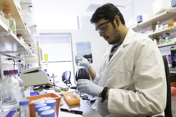A researcher in a wet lab handles a pipette and other equipment while wearing lab equipment