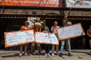 student scholarship recipients holding large checks with hook 'em mascot and UT President Jay Hartzell