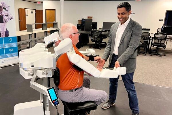 The author sits with arms strapped to white robot as professor stands