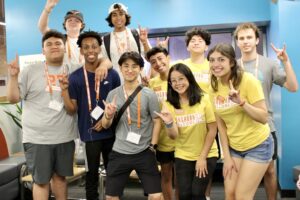 group of students posing for camera smiling and holding hook 'em hand signal