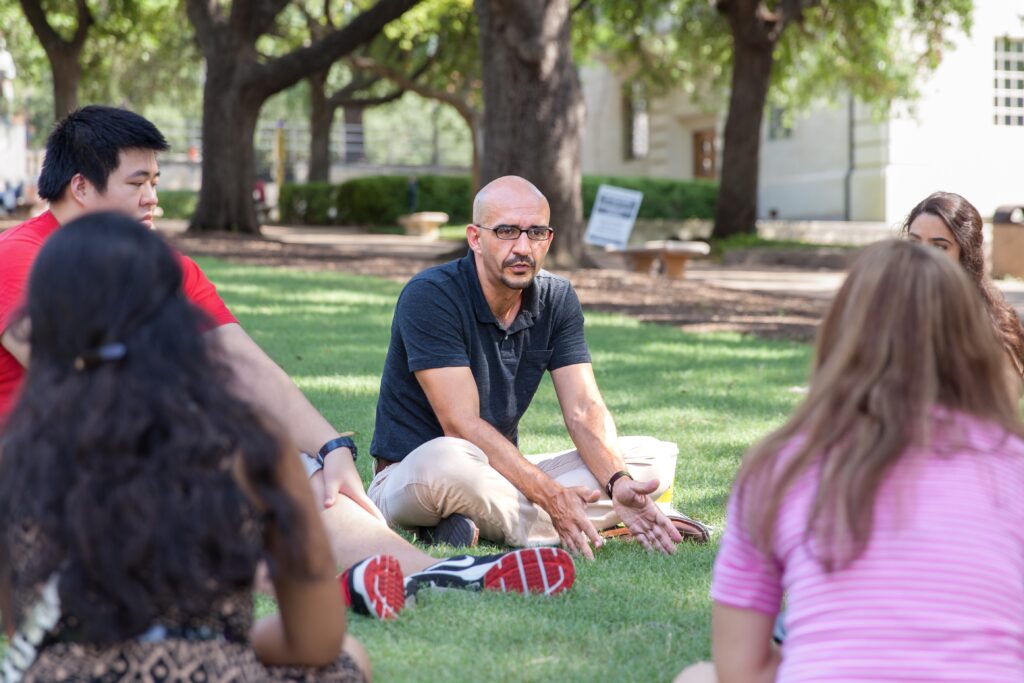professor sits on the lawn with students in a discussion session