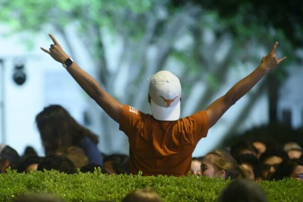 student standing in crowd holding hook 'em hand signal wearing burnt orange