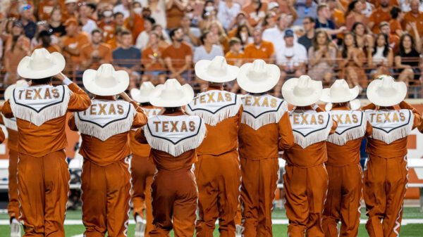 Members of the Longhorn Band with TEXAS across the back of their uniforms marching away from the camera
