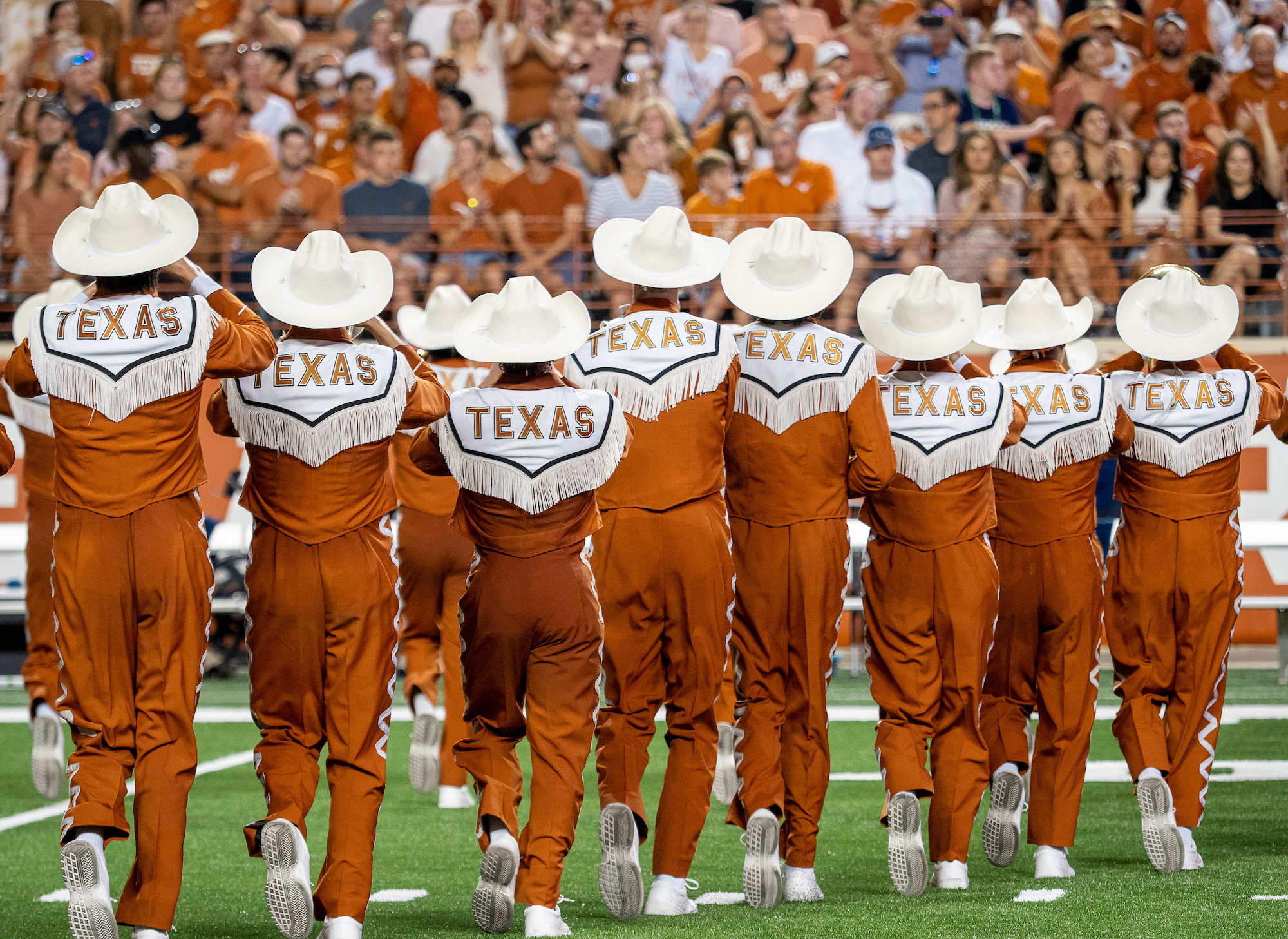 Members of the Longhorn Band with TEXAS across the back of their uniforms marching away from the camera