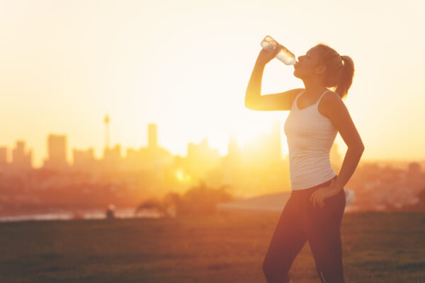 Silhouette of a woman drinking form a cold water bottle.