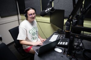 Student in front of a microphone and computer in podcast production course