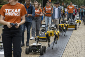 students walking with controllers in hand next to robots they are controlling