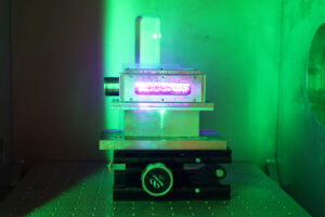 A piece of scientific equipment lit from the outside by green light. In a window in the side of the equipment, a pink light glows.