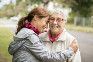 An elderly woman with red framed eye glasses, right, is embraced by a younger woman on the left.