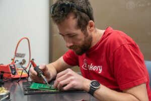 person with red t-shirt soldering onto a circuit board