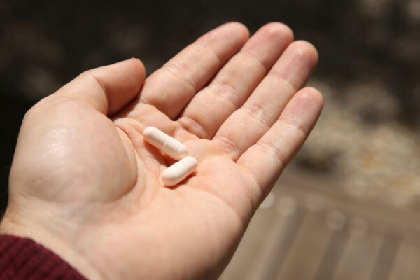A hand holding two white pills