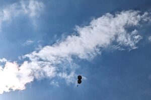 view from ground of sky and clouds with balloons floating in air