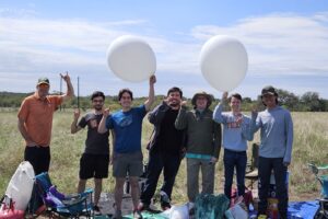 group of students posing in a field with balloons for texas eclipse ballooning project