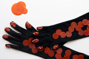 White background with a pair of black gloves covered in orange sequins
