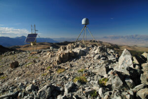 Photo of a tripod-mounted GPS sensor and solar panel installed on a mountain top.