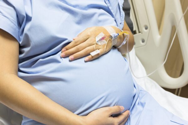 Asian Pregnant Woman patient is on drip receiving a saline solution on bed VIP room at hospital.