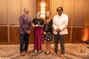 Four people posing for a photo, one of whom is holding a glass award