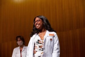 Brianna Earskine stands, smiling in white lab coat