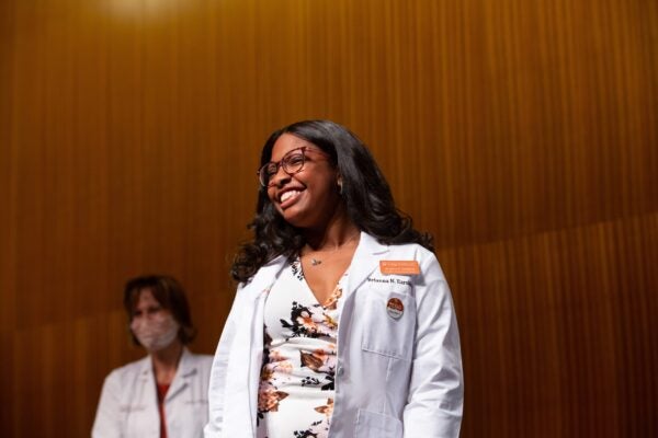 Brianna Earskine stands, smiling in white lab coat